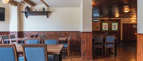 Interior de restaurante con mesas y sillas de madera, techo de madera y estanterías en la pared.