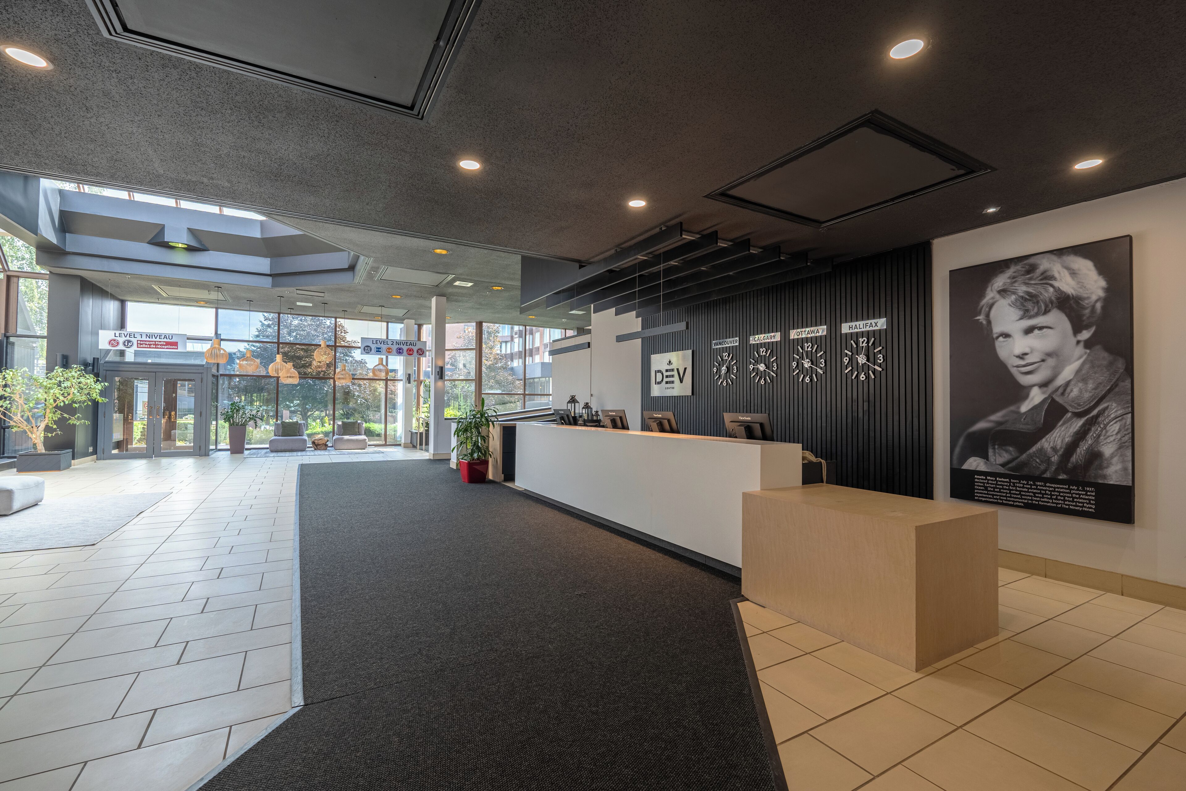 A modern reception area with a reception desk, potted plants, and a large poster on the wall.
