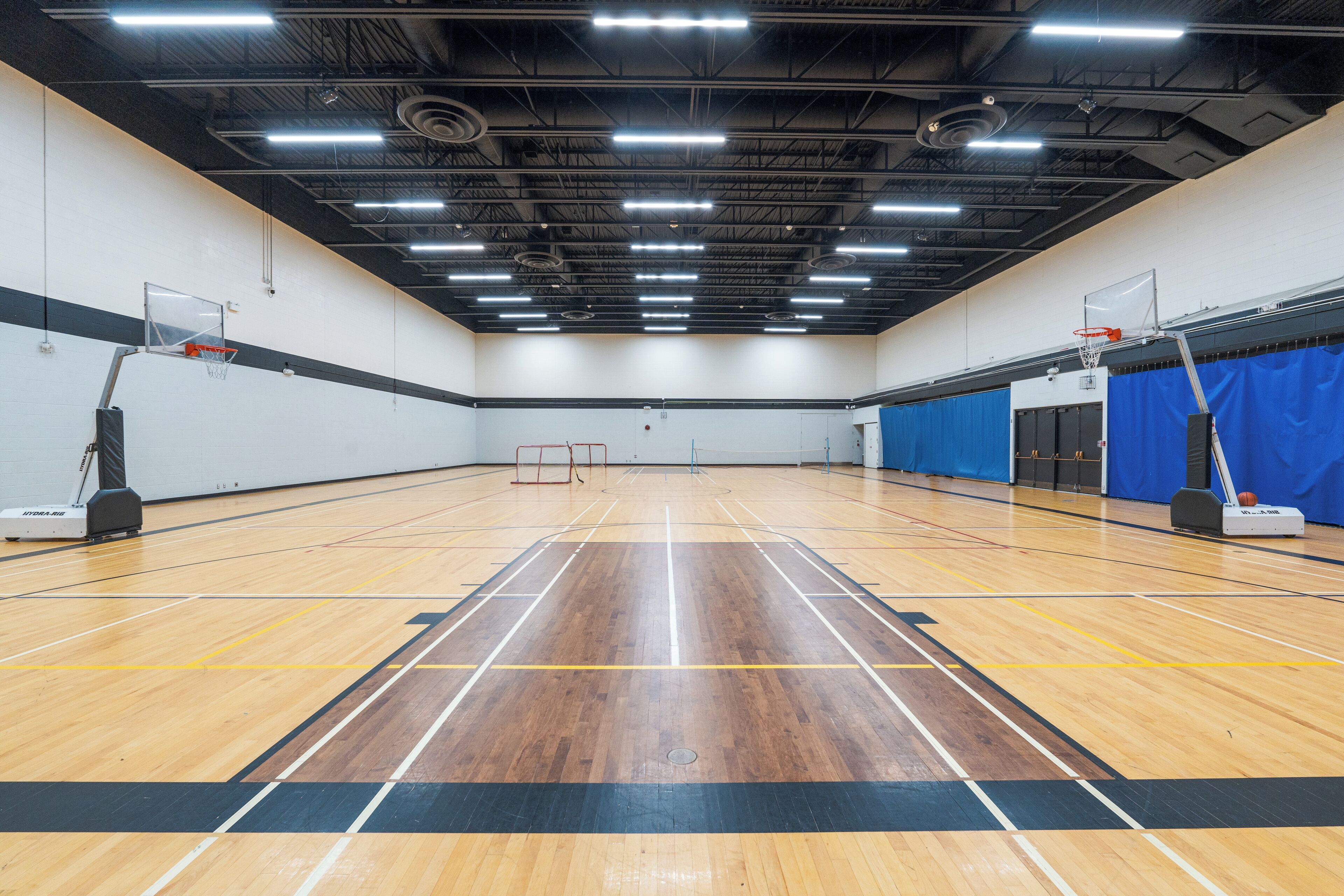 An indoor basketball court with wooden flooring, two basketball hoops, and overhead lighting.