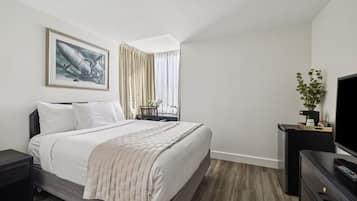 A modern bedroom with a large bed, a TV, a desk, and a plant.