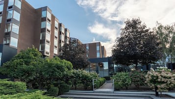 Un edificio moderno de varios pisos, rodeado de abundante vegetación y un cielo despejado.