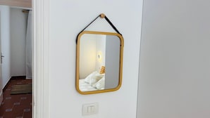 Een kamer met een spiegel aan de muur, een deur en een lichtschakelaar.