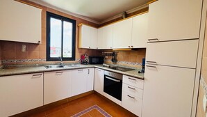 Een kleine keuken met witte kastjes, een ingebouwde magnetron, een fornuis en een spoelbak.