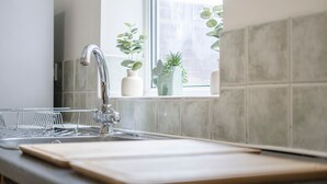 Eine Küche mit Spüle aus Edelstahl, Schneidebrett und Blumentöpfen am Fensterbrett.