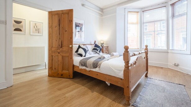 Ein Schlafzimmer mit einem hölzernen Bett, einem weißen Heizkörper und einem großen Fenster mit Jalousien.