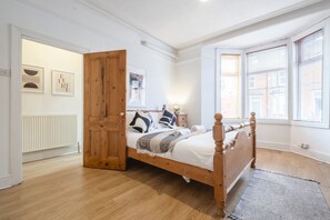 A bedroom with a wooden bed, a white radiator, and a large window with blinds. - Cosy Flat,Great Location&Parking (West Jesmond)