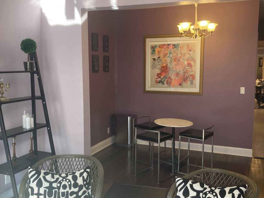 A living room with two wicker chairs with patterned cushions, a small round table, a chandelier, a framed floral painting on the wall, and a dark wooden floor.