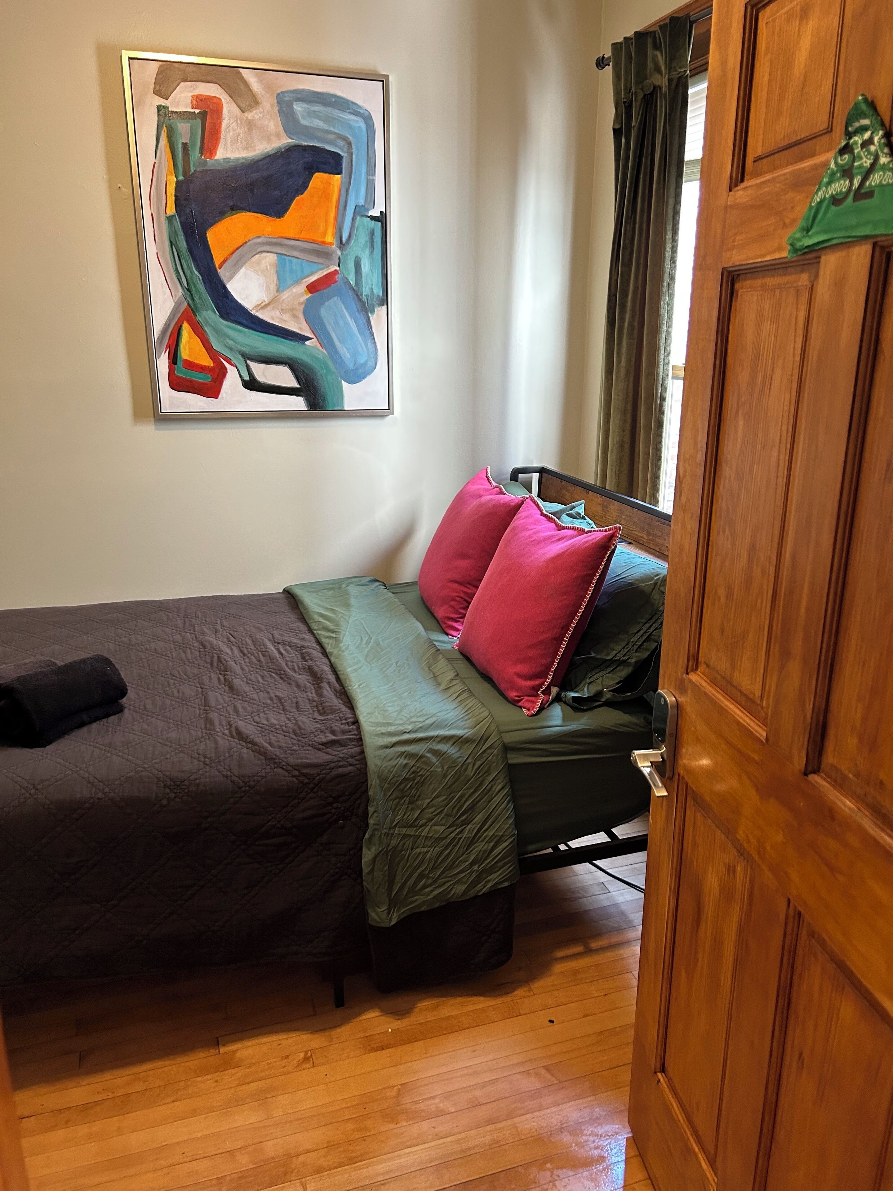 Une chambre à coucher avec un lit, des oreillers, une couverture verte, une porte en bois et un tableau accroché au mur.