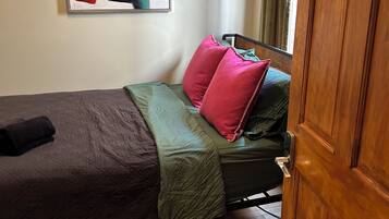 Une chambre à coucher avec un lit, des oreillers, une couverture verte, une porte en bois et un tableau accroché au mur.