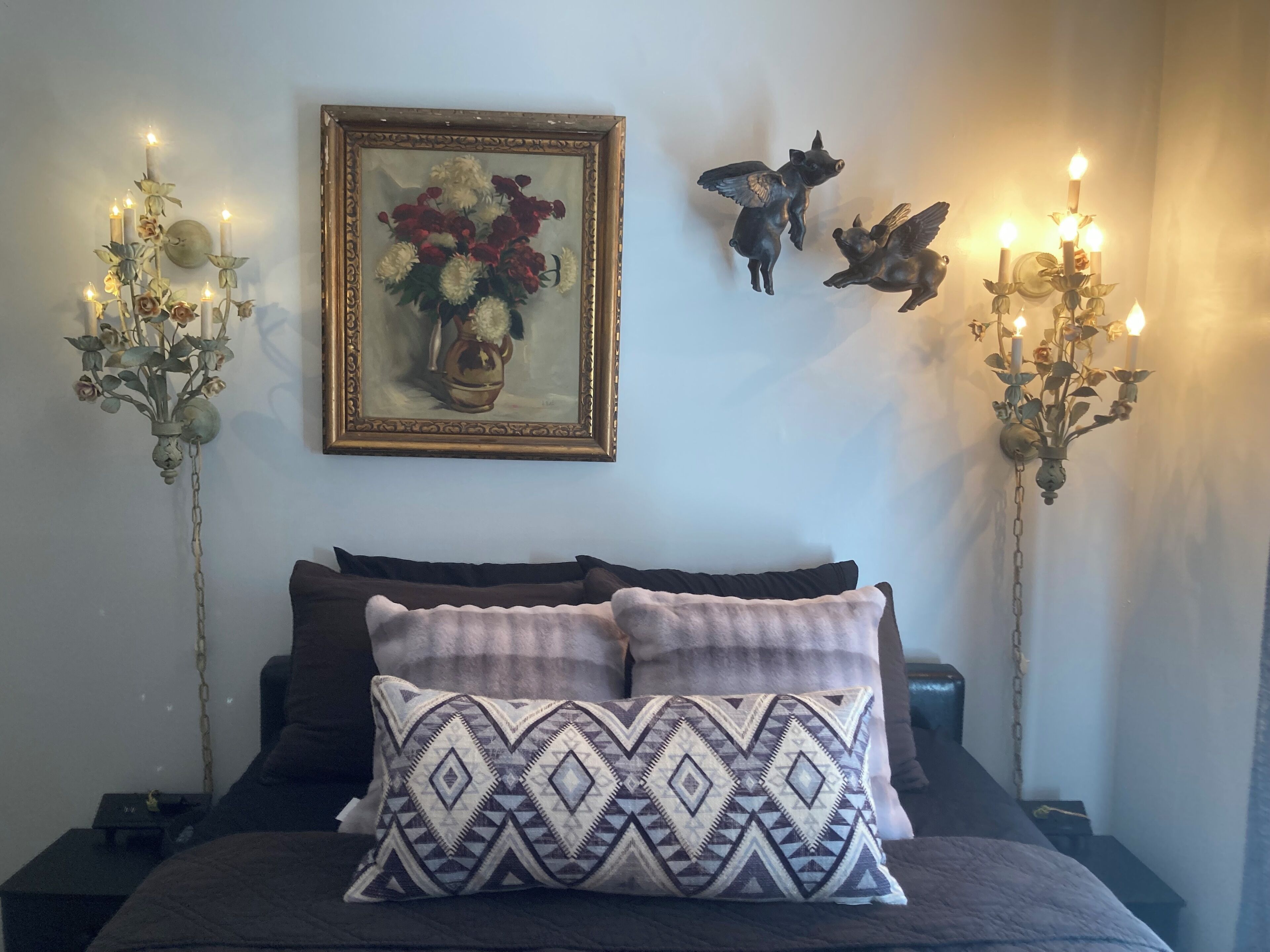 Un dormitorio con una cama, dos lámparas fijadas a la pared, un cuadro enmarco y una escultura decorativa de un cerdo.