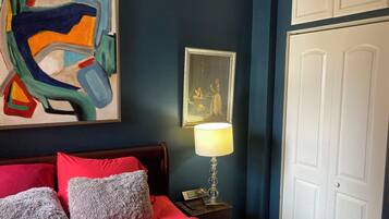 A bedroom with a bed, red and grey pillows, a painting, a lamp, and a framed picture on the wall.