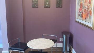 A dining area with a round table and four chairs, a chandelier, framed wine glass illustrations on the wall, and a trash can.