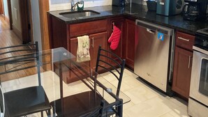 A modern kitchen with wooden cabinets, a stainless steel dishwasher, a coffee maker, and a glass dining table with chairs. - Dorothy's (Chicago)