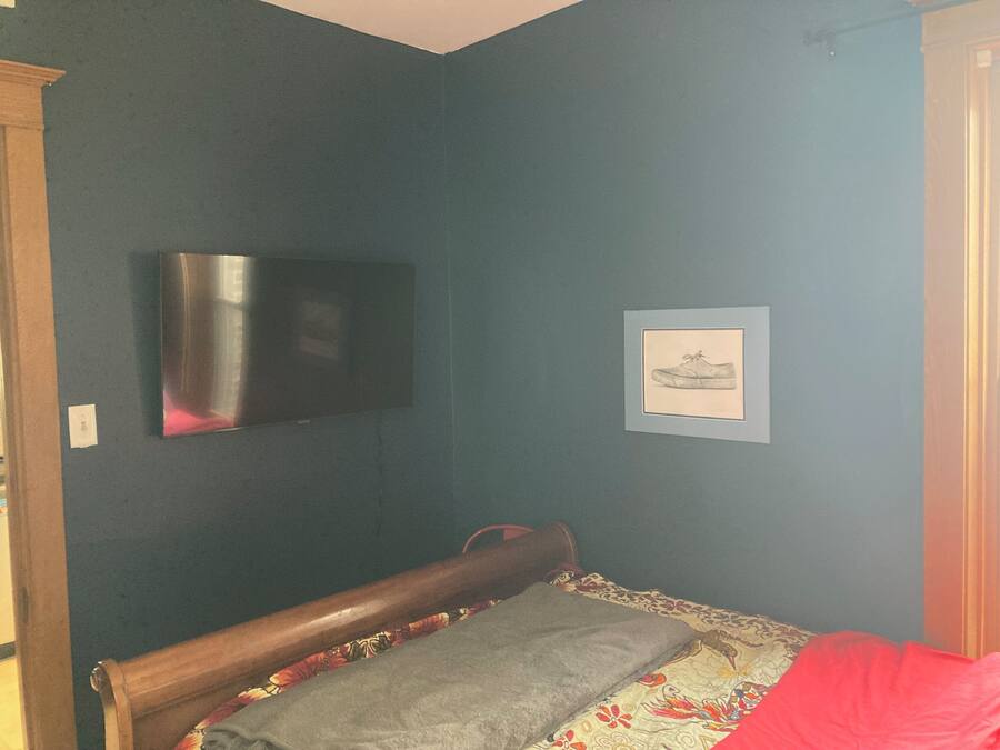 Quarto com uma cama, televisão na parede e um quadro emoldurado.