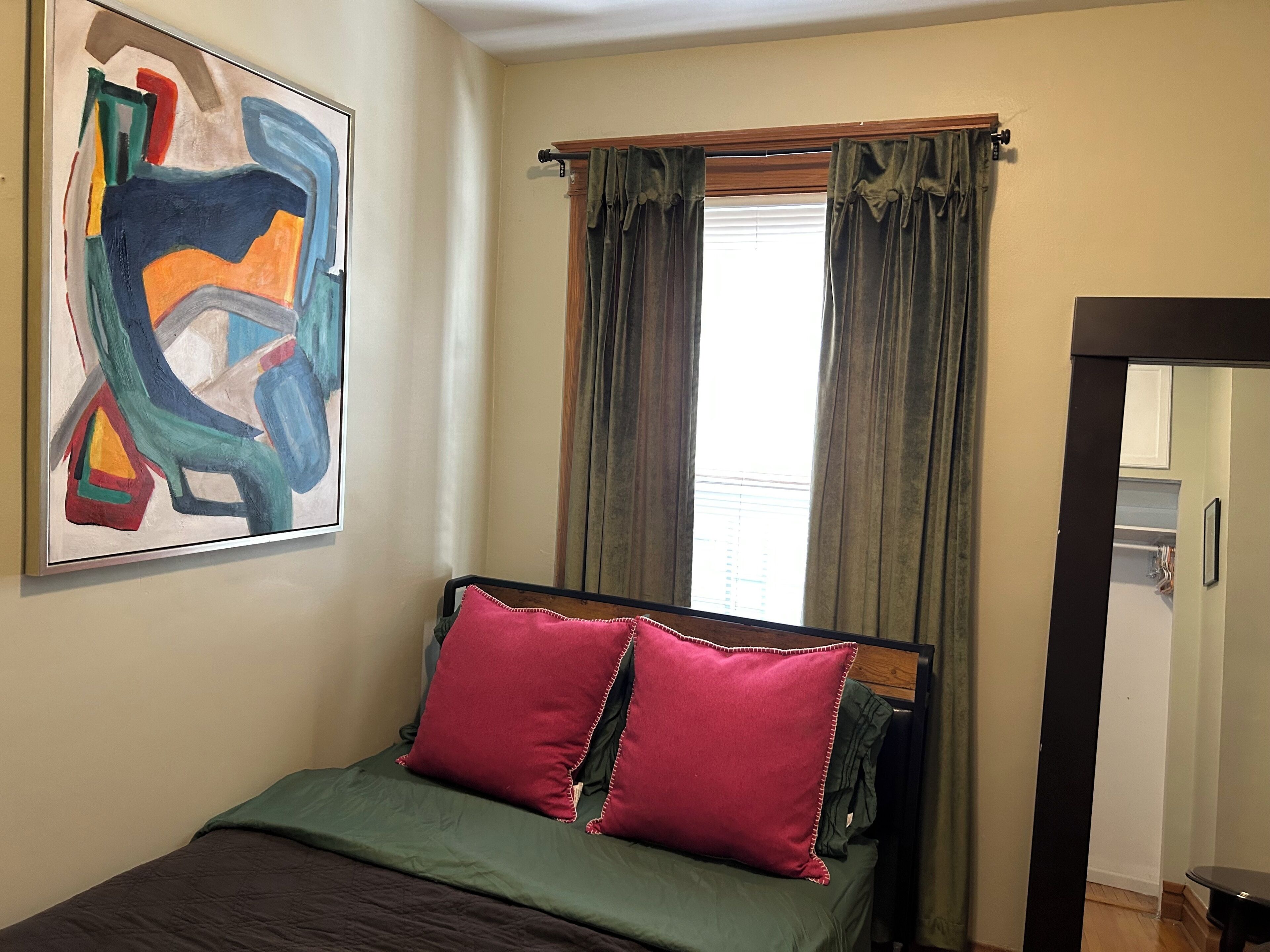 Une chambre à coucher avec un lit, un tableau et une fenêtre avec des rideaux.