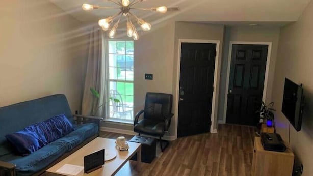 A living room with a blue sofa, a wooden coffee table, a black chair, a ceiling light fixture, and a door.