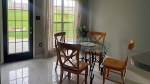 A dining area with a glass table, wooden chairs, and a ceiling light fixture.