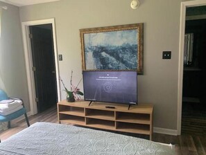 Une chambre d’hôtel avec un lit, un téléviseur posé sur un meuble en bois, un tableau encadré au mur et une porte sur le côté gauche.