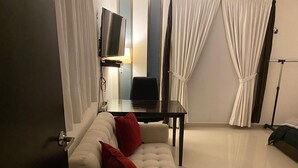 Ein modernes Wohnzimmer mit einer Couch, roten Kissen, einem Fernseher, einem kleinen Tisch und Vorhängen.