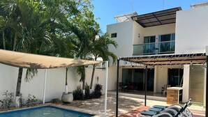 Ein modernes Haus mit Swimmingpool, einer überdachten Terrasse mit Liegestühlen und einem gepflegten Garten.
