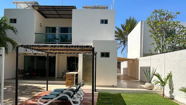 Ein modernes Haus mit überdachter Terrasse, Pool und gepflegtem Rasen.