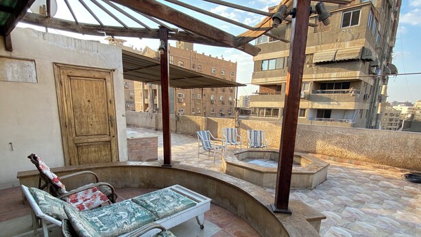 A rooftop terrace with a covered seating area, a hot tub, and a view of surrounding buildings. - Vintage Rooftop (Heliopolis)