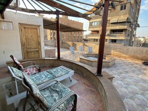 Una terrazza sul tetto con una zona salotto coperta, una vasca idromassaggio e vista sugli edifici circostanti.