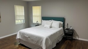 A bedroom with a bed, two bedside tables, a nightstand, and two windows with blinds. - Cozy 1-bedroom in charming Durham (Durham)