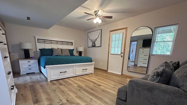 A bedroom with a bed, nightstands, a dresser, a ceiling fan, and a large mirror. - Harmony Haven (Saint Robert)