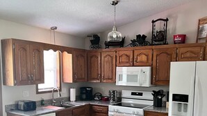A kitchen with wooden cabinets, a white refrigerator, a microwave, a stove, and a dishwasher. - Harmony Haven (Saint Robert)