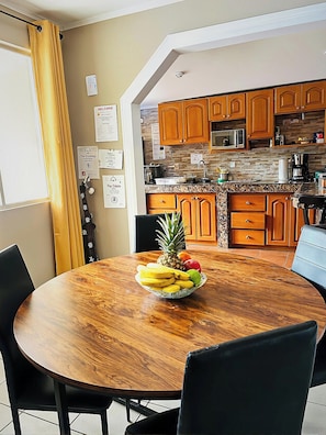 A dining area with a wooden table, chairs, and a fruit bowl. - Private residential home for 8 with private pool; 5 min walk to Jacó Beach. (Jaco)