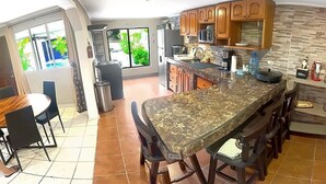 A modern kitchen with a large island, wooden cabinets, and a dining area with chairs.