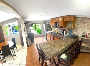 A modern kitchen with a large island, wooden cabinets, and a dining area with chairs.