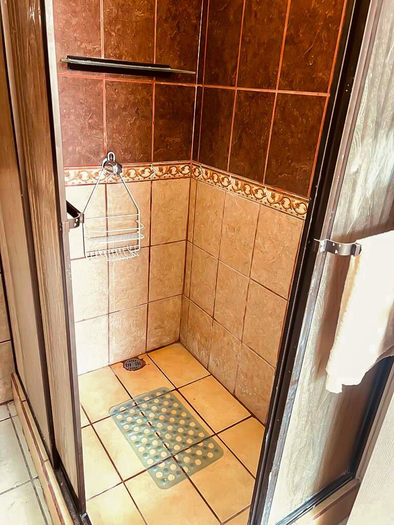 A small, tiled shower room with a metal rack and a drain.