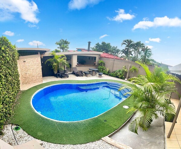 A swimming pool with a curved edge, surrounded by a well-maintained lawn and palm trees.