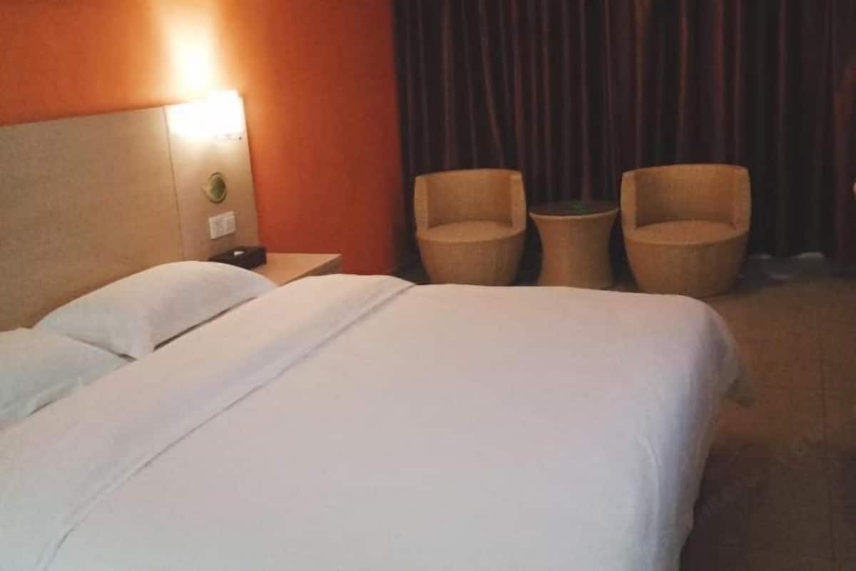 A hotel room with a bed, two chairs, a small table, and a nightstand with a lamp.