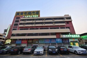 A multi-story building with a parking lot in front, featuring several commercial signs and parked cars.