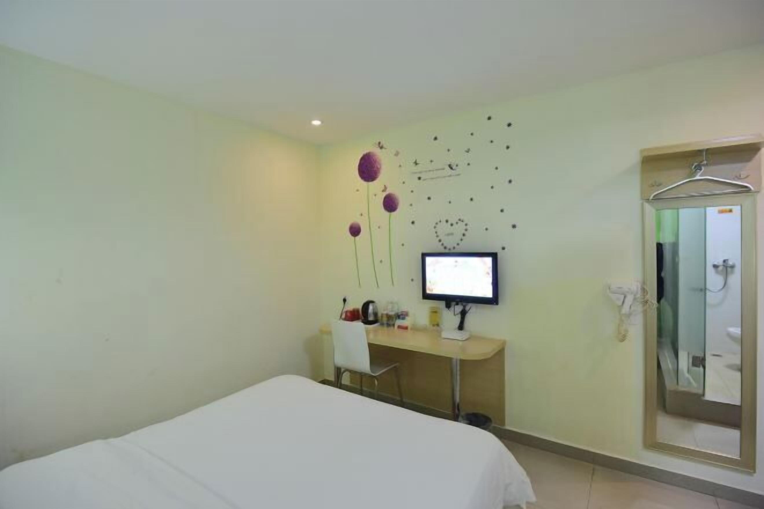 Habitación de hotel con cama, escritorio con computadora, espejo y zona de ducha.