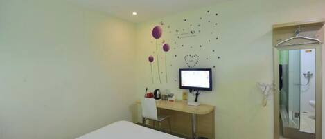 Habitación de hotel con cama, escritorio con computadora, espejo y zona de ducha.