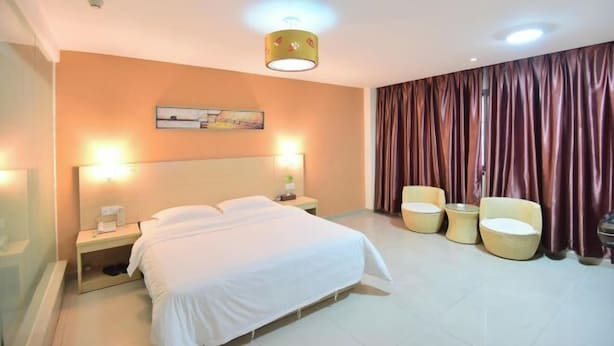 A hotel room with a bed, bedside lamps, a nightstand, a painting on the wall, and a curtain. - Liudianban Inn (Dongguan Dalang) (Dongguan)