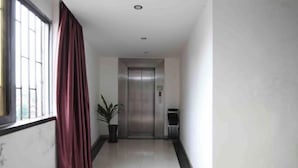 A corridor with a red curtain, a potted plant, and an elevator. - Liudianban Inn (Dongguan Dalang) (Dongguan)