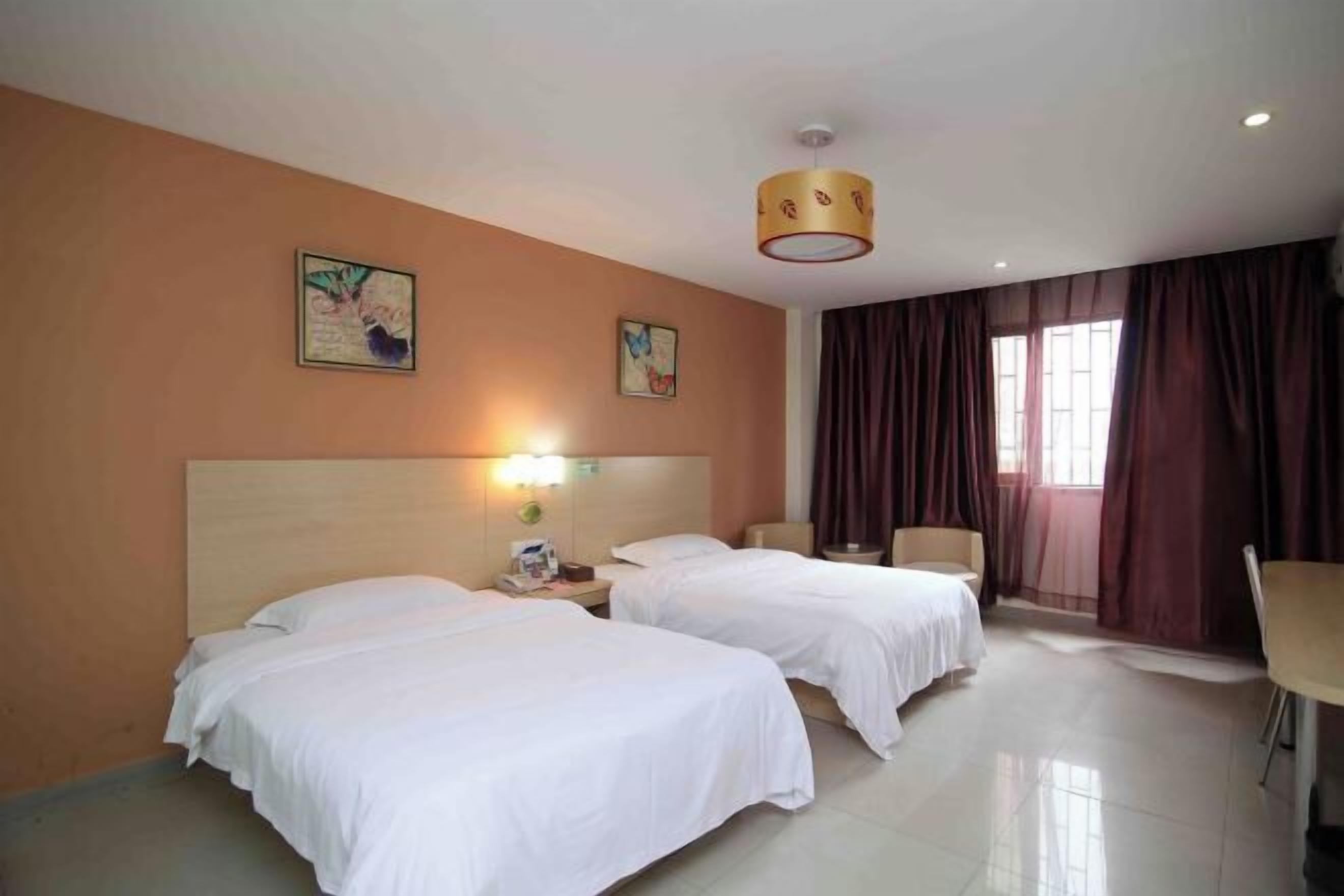 A hotel room with two beds, a desk, a chair, and a large window with curtains.