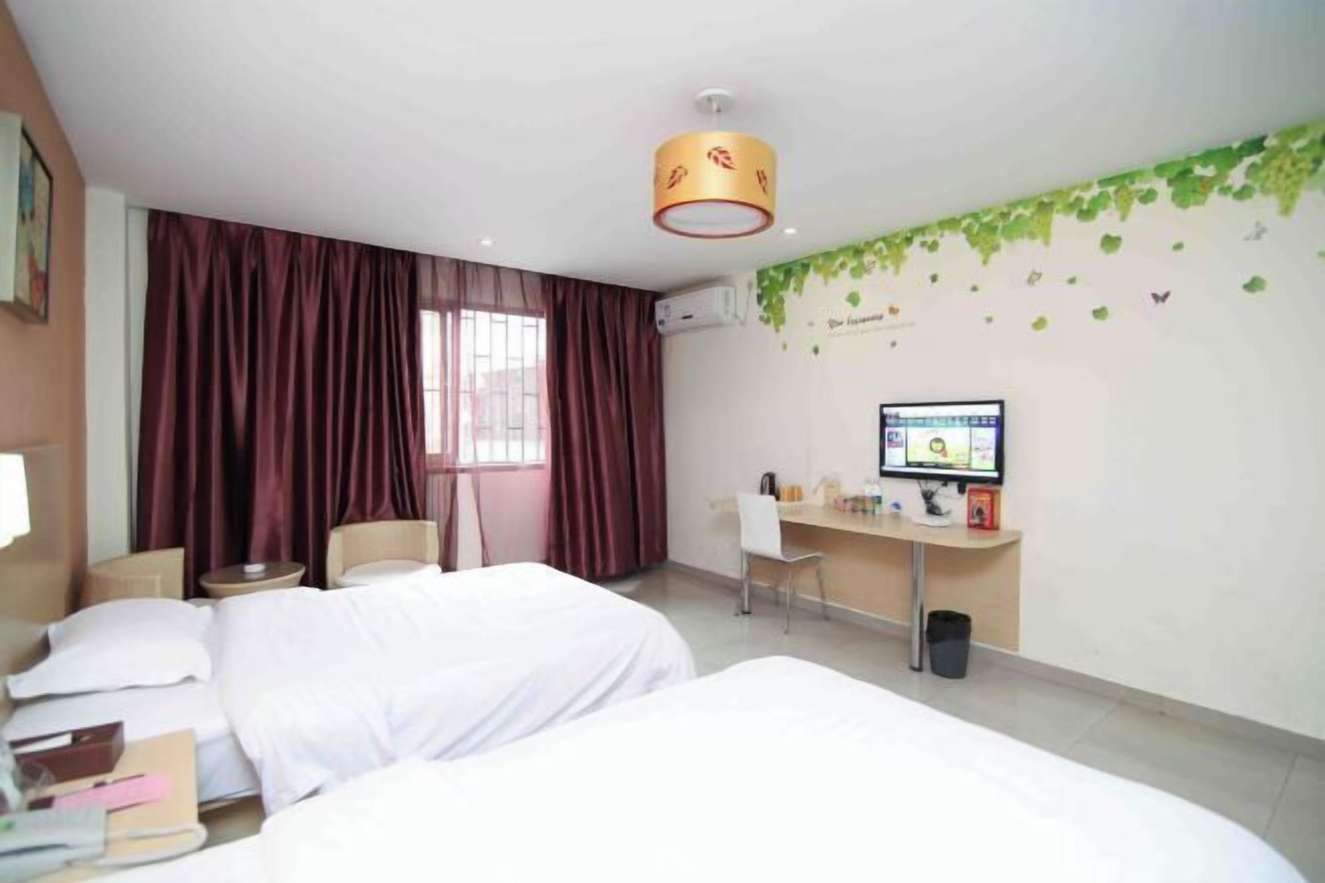 A hotel room with two beds, a desk with a computer, a chair, and a window with curtains.