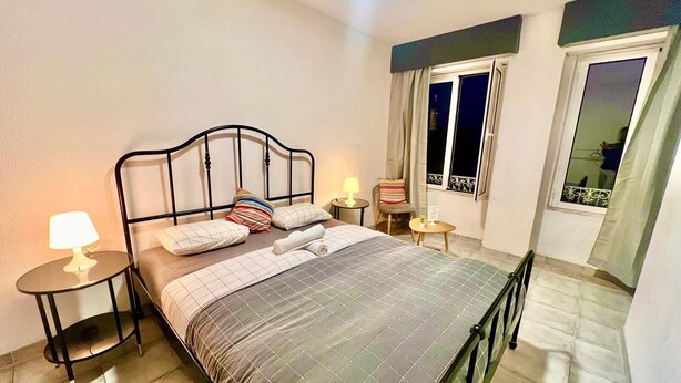 Ein ordentlich eingerichtetes Schlafzimmer mit Bett, Nachttischen, einem Sessel und einem Fenster mit Vorhängen.