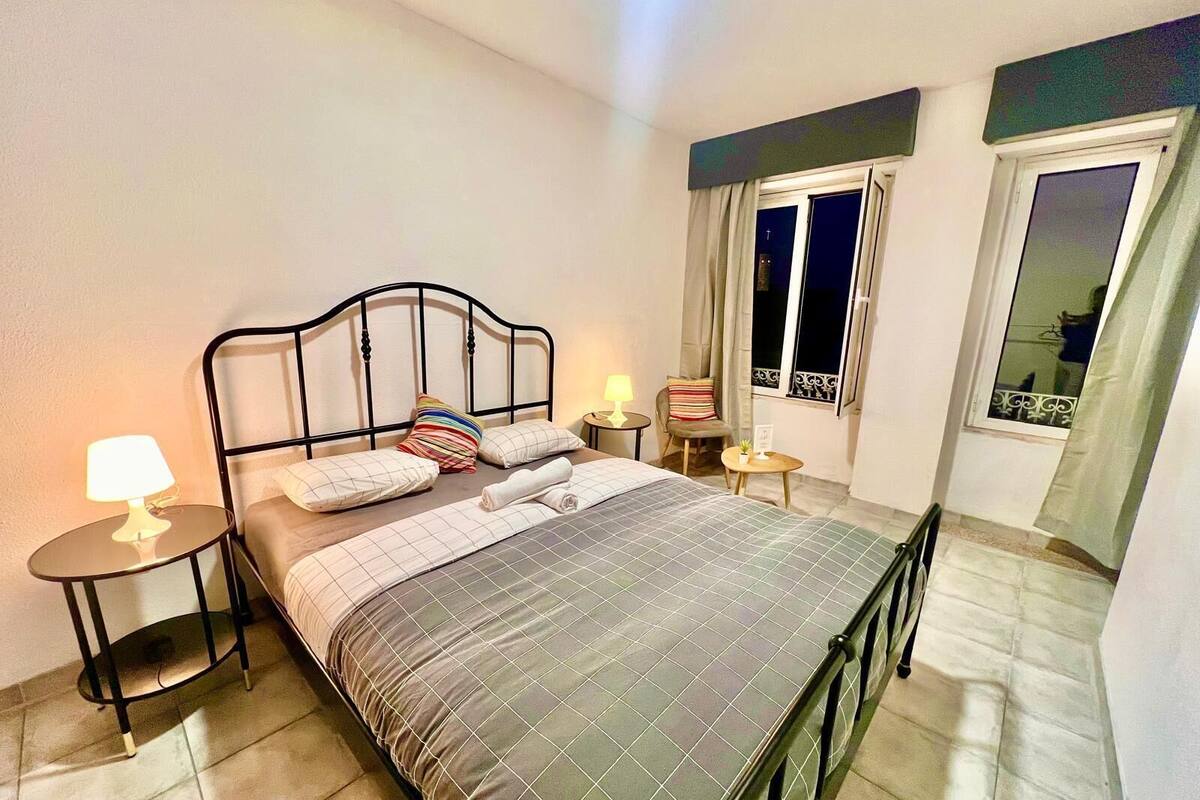 A neatly arranged bedroom with a bed, bedside tables, a chair, and a window with curtains.