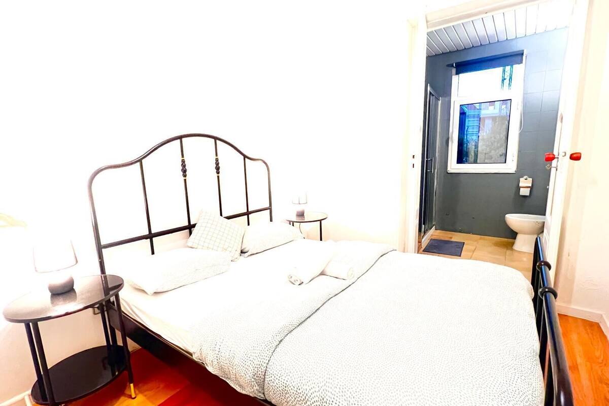 A neatly made bed with a headboard, two bedside tables, and a window with a view of the outside.