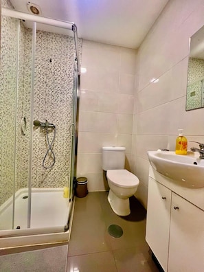 Un baño con ducha de vidrio, inodoro y lavamanos con espejo.