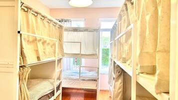 Ein Zimmer mit Etagenbetten, einem mit Vorhängen versehenen Fenster, Holzboden und einer Pendelleuchte.