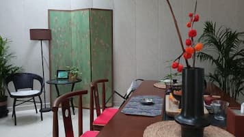 Uma área de refeições com mesa de madeira, cadeiras, um vaso com flores vermelhas e um painel verde.
