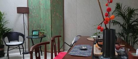 A dining area with a wooden table, chairs, a vase with red flowers, and a green partition.